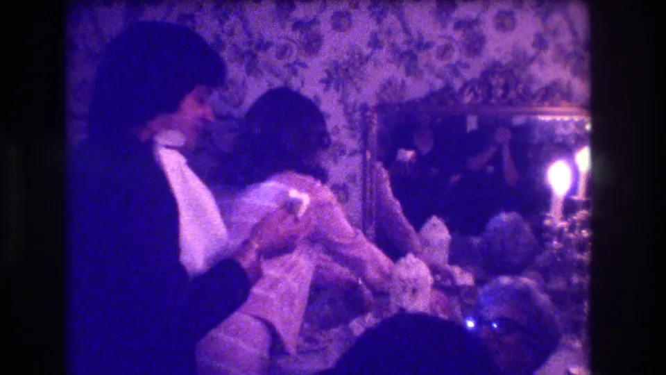 At the Medford wedding reception, the tuxedoed man bends over the seated woman while guests and candlelight fill the dim room.
