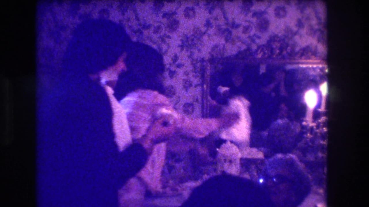 Two adults in formal clothing sit close together in a dim purple-lit room.
