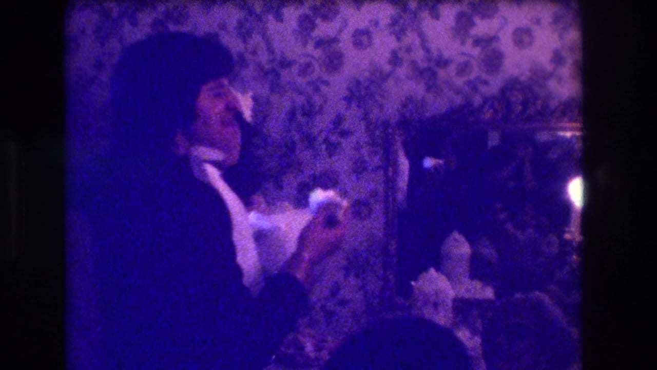 A formally dressed adult leans toward another person near a table and wall mirror.