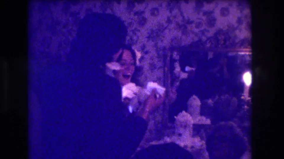 The 8mm frame shows a dark-clothed adult leaning toward a seated person at a formal indoor gathering in Medford, New Jersey.