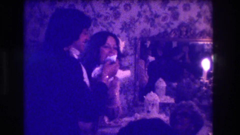 1973 Medford, New Jersey home-movie frame showing a bride and groom by the cake table in a purple-tinted reception interior.