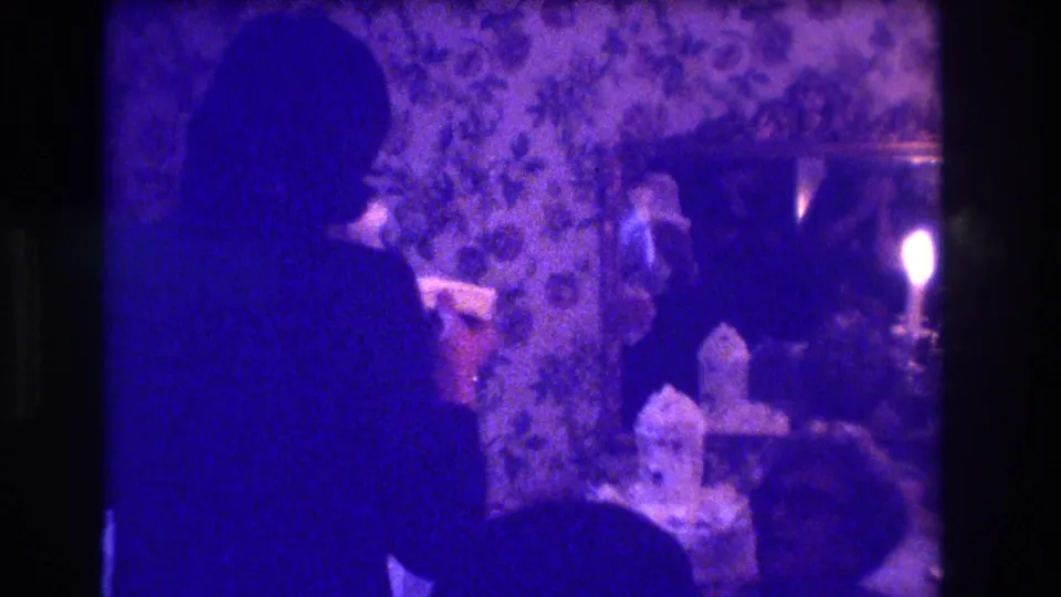 1973 Medford wedding reception frame with a standing figure near the cake table, candlelight, seated guests, and floral wallpaper.