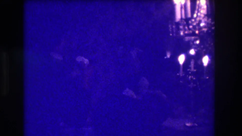 The closing 1973 Medford frame is very underexposed, showing candle-style lights and faint silhouettes in a private interior.