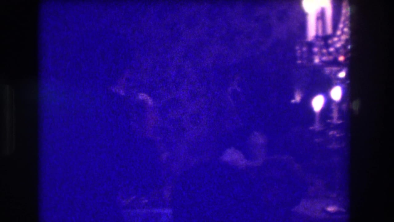 Dim blue-toned indoor party scene with shadowed adults near candlelit fixtures.