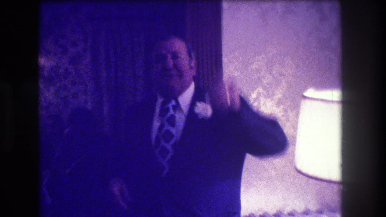 The suited man appears to gesture while standing near a lamp in the Medford wedding reception interior.
