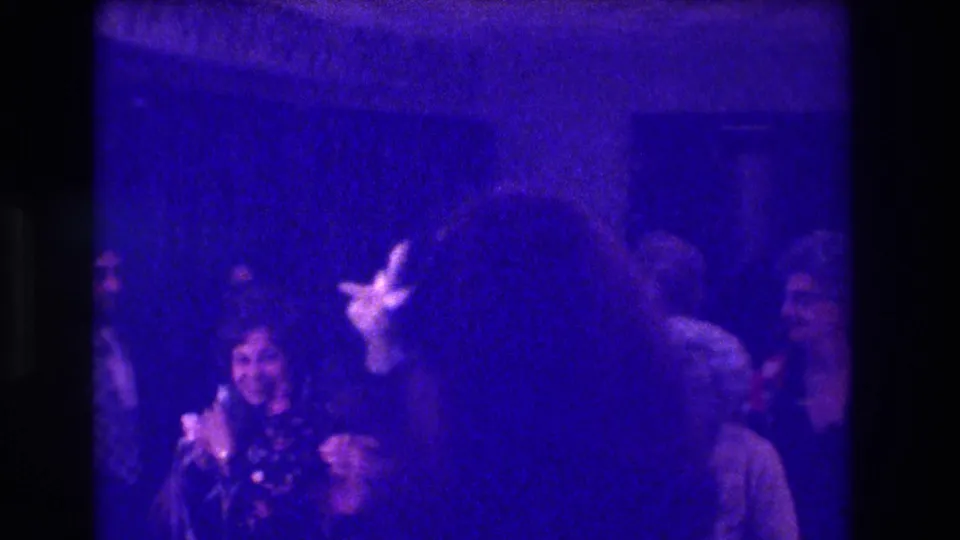 Handheld 8mm view of 1973 Medford wedding reception guests watching a woman near the bouquet, with blue-purple color shift.