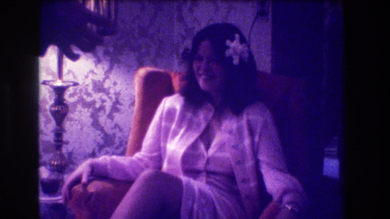 Woman smiles in an armchair as a hand enters near the top of the frame.