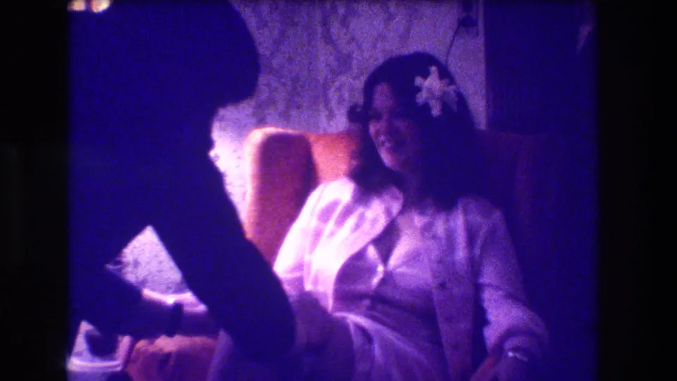 Final 1973 Medford wedding reception frame with the seated bride smiling as the suited man bends over the garter area.