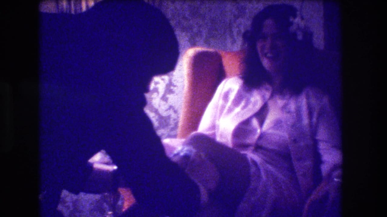 Bride in a white gown smiles from a chair beside a dark silhouetted figure in the foreground.