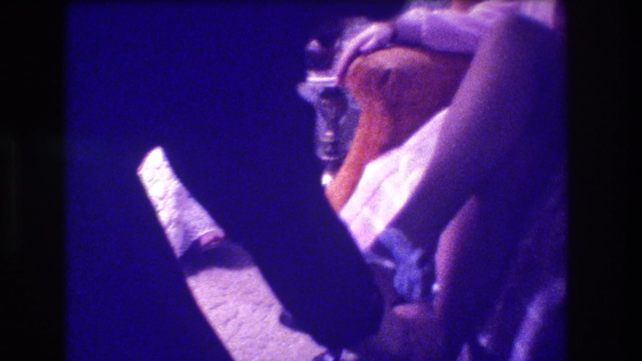 A man leans near a seated woman's leg as her gartered stocking and white shoe are visible.