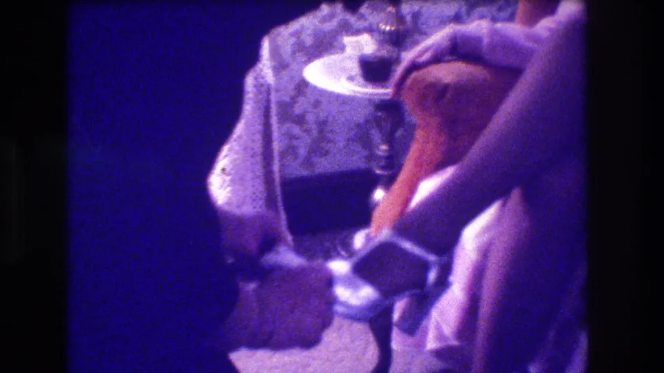 1973 Medford 8mm frame showing the woman seated beside a small table and ornate chair while hands work near her gartered leg.