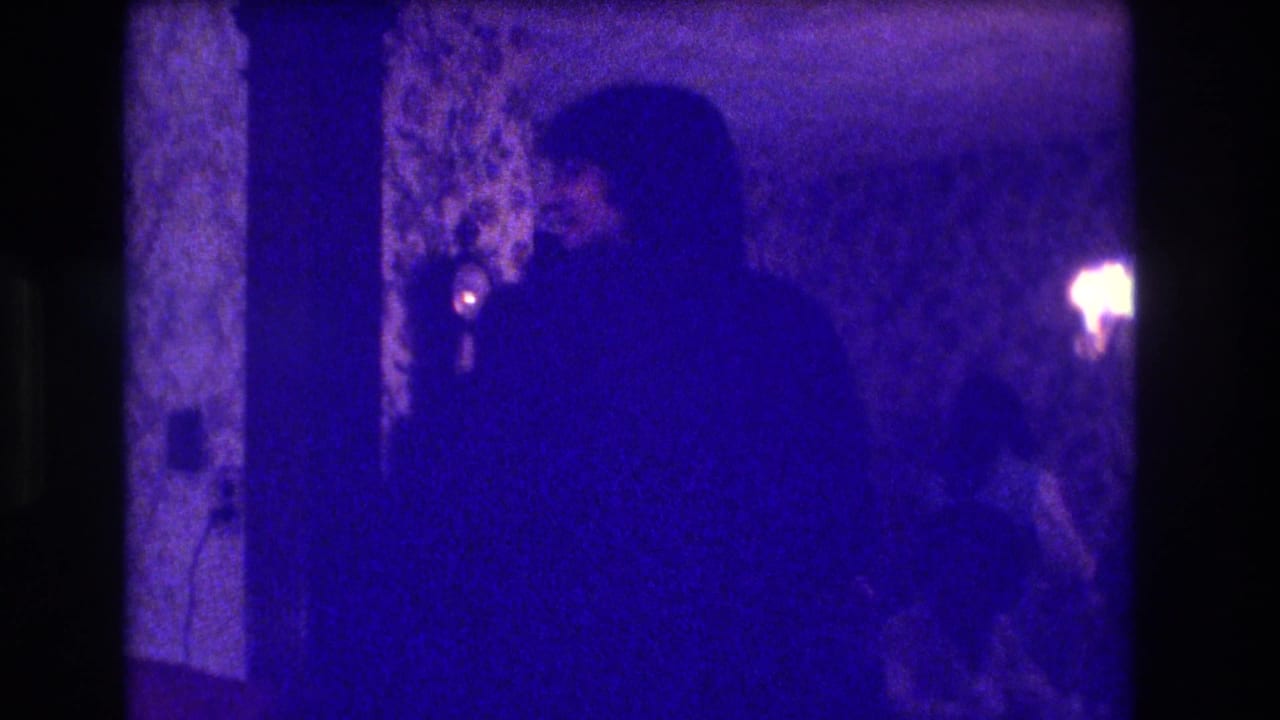 Silhouetted adults in a dim dining room with patterned wallpaper and blue-purple film cast.