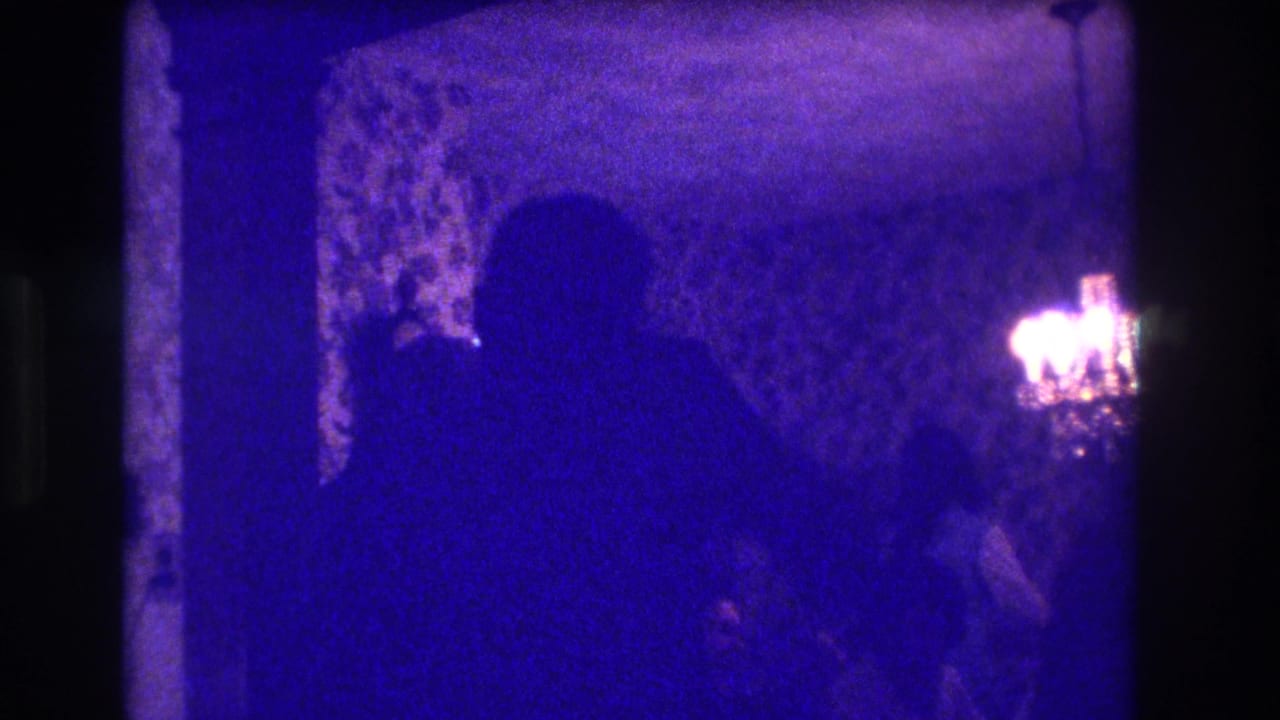 Low-light 1973 Medford interior frame with adults in silhouette near patterned wallpaper and a bright light source on the right.
