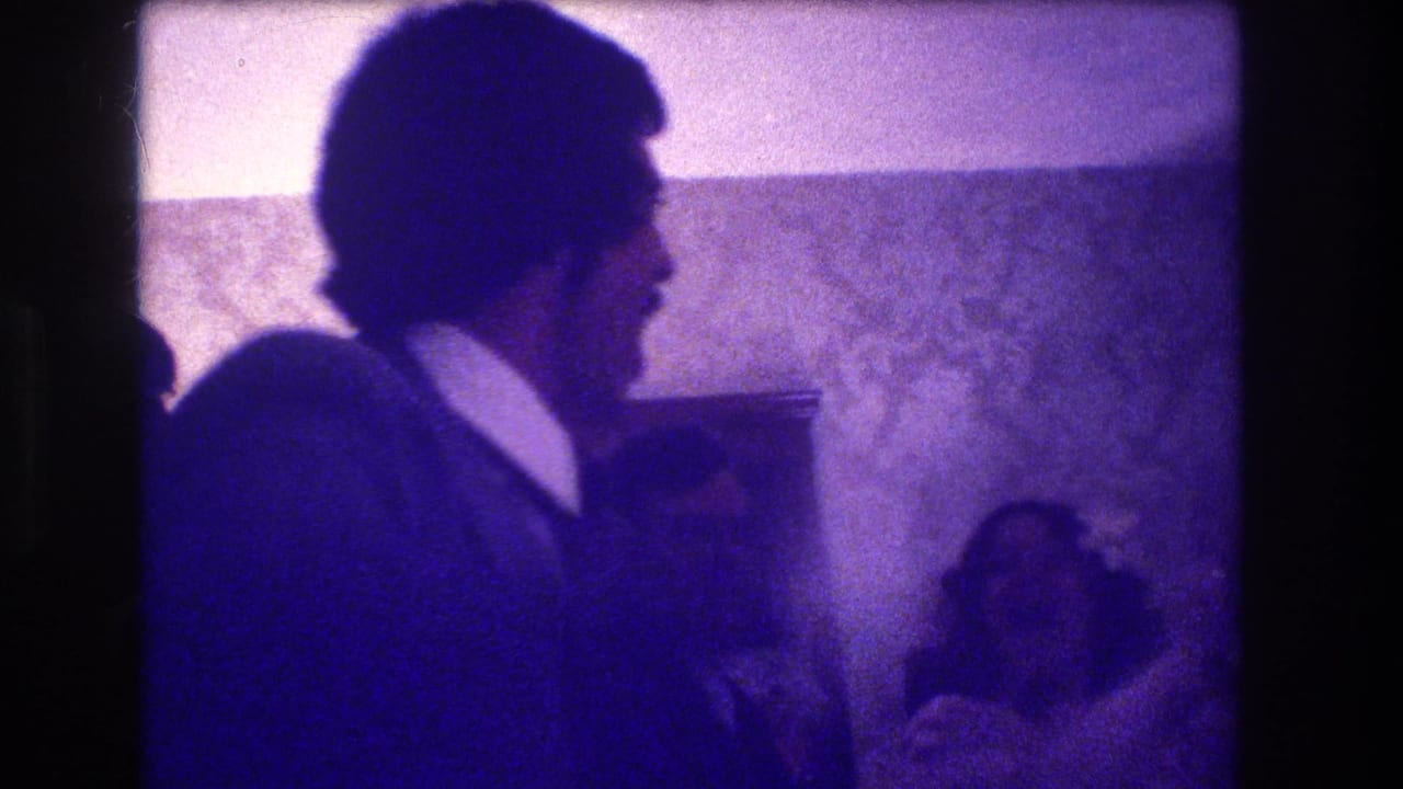 1973 Medford, New Jersey home-movie frame showing a man in profile clapping while other guests sit nearby in a private interior.