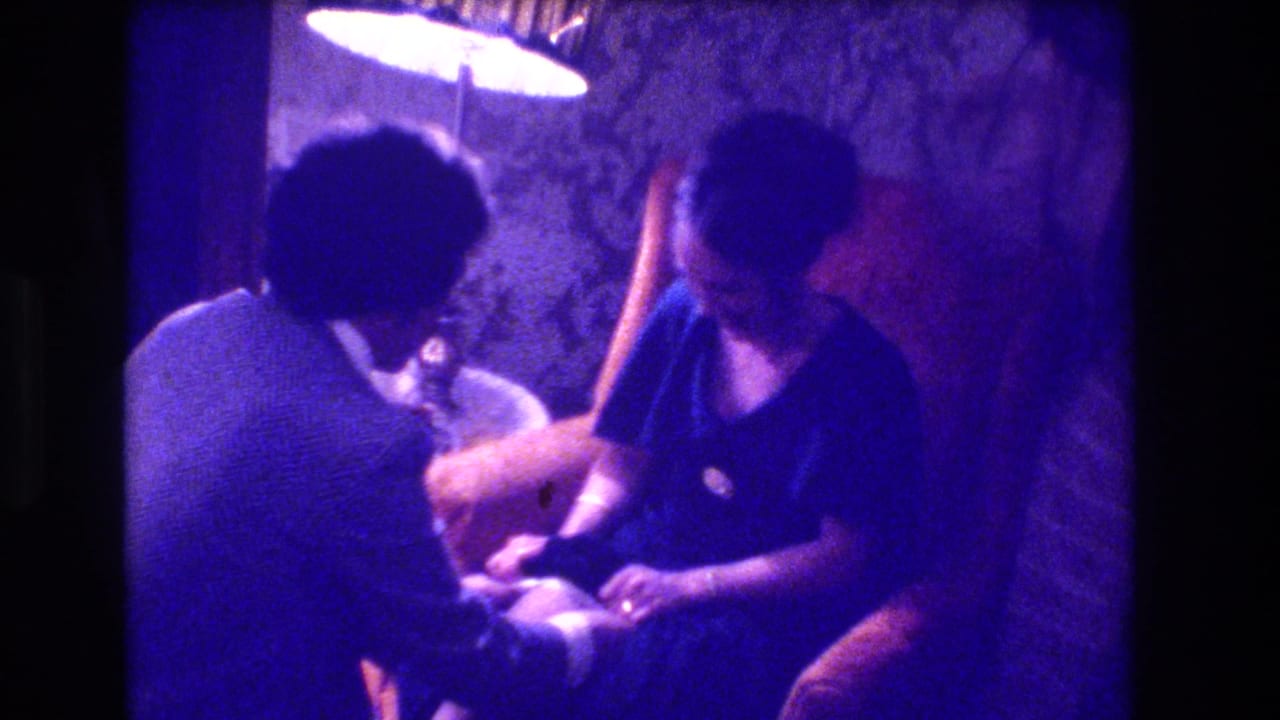 Man seen from behind in a light top, seated beside a woman in a dark top; round lamp above, textured wall behind.