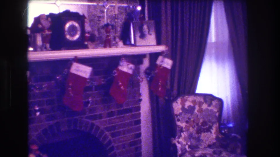 1973 Medford, New Jersey home interior showing a holiday mantel with red stockings, a framed portrait, dark curtains, bright window light, and a floral armchair.