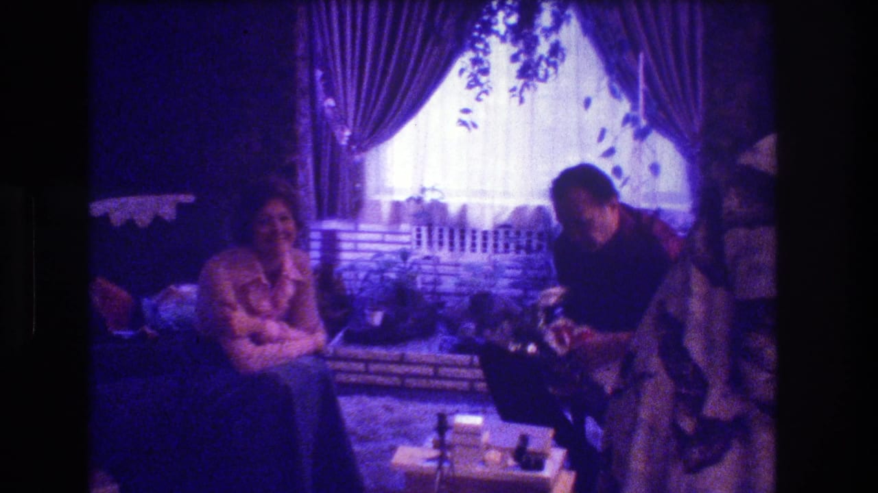 Woman seated while a man leans in beside her in a decorated living room.