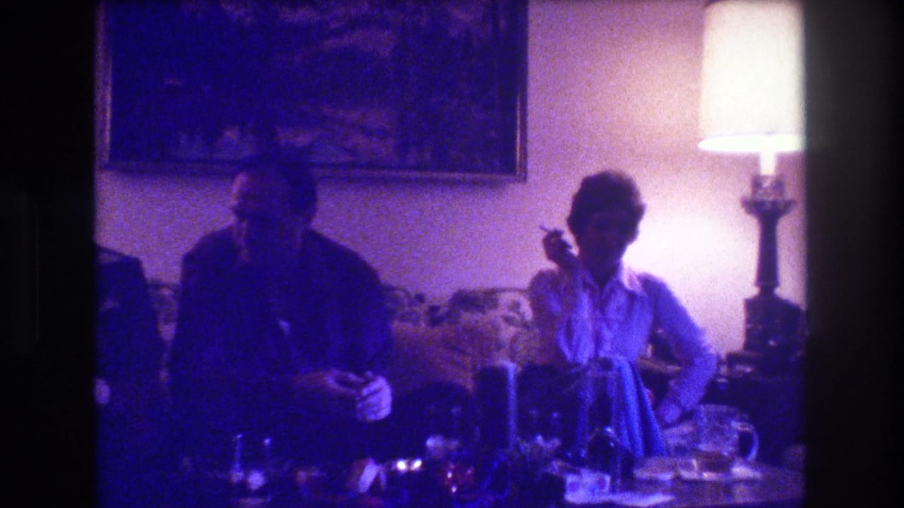 Two adults seated in a dim living room beside a glowing table lamp.