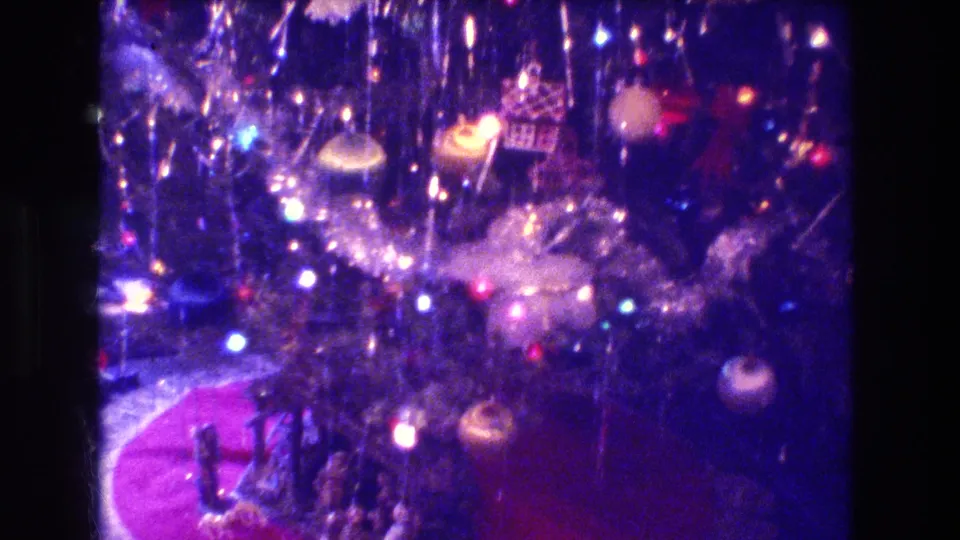 1973 Medford, New Jersey 8mm frame looking into the lit Christmas tree, with ornaments, bright colored bulbs, a red circular rug, and small figures below.