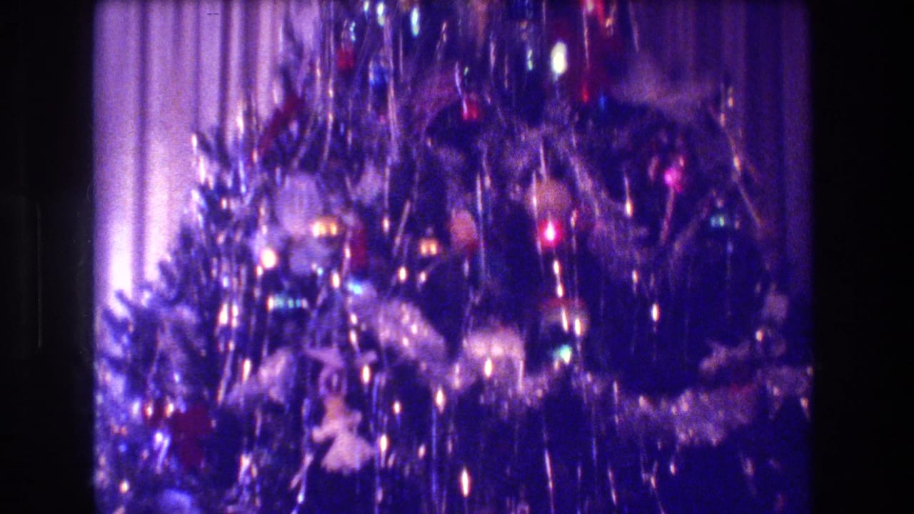 Decorated Christmas tree with tinsel, ornaments, and bright lights beside curtains.