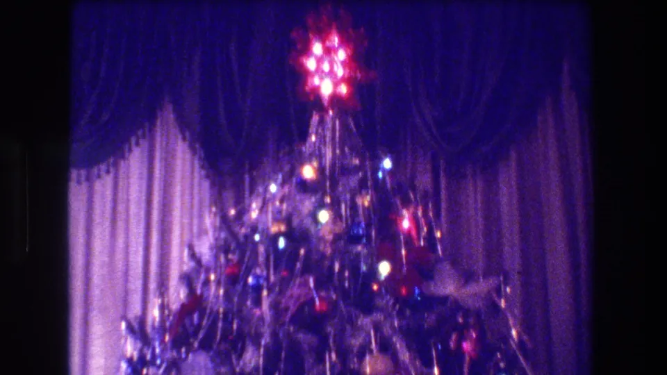 1973 Medford, New Jersey home interior frame showing a lit Christmas tree rising in front of curtains, with dense tinsel and visible film grain.