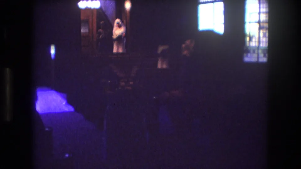 1974 Boston wedding footage frame with the bride standing near the altar, bright stained-glass windows at right, and guests barely visible in the low light.