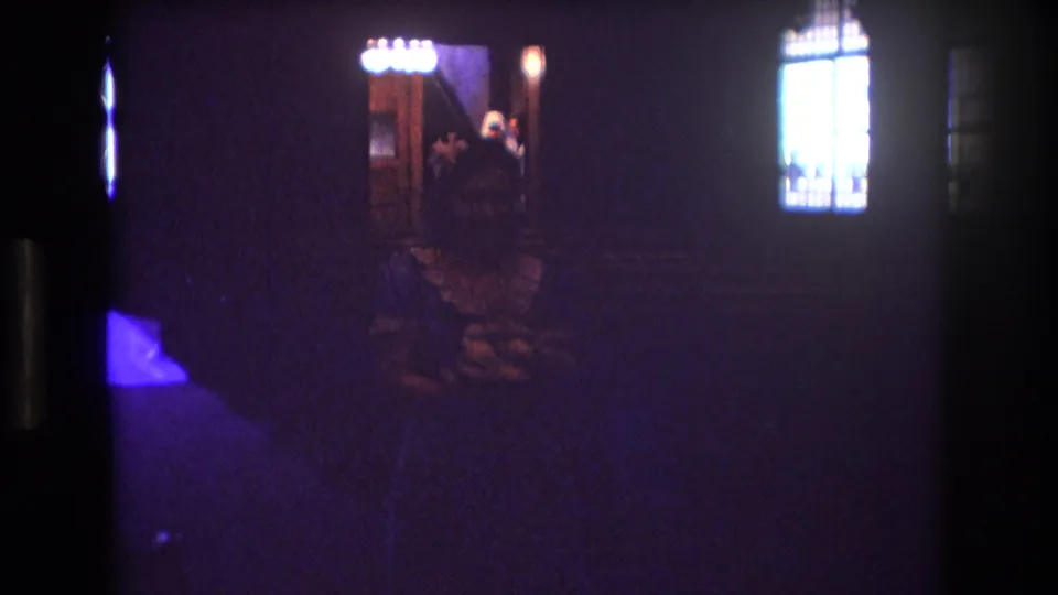 1974 Boston 8mm frame of a church wedding ceremony, with the bride near the altar, a seated guest in the foreground, and stained-glass windows glowing in the darkness.