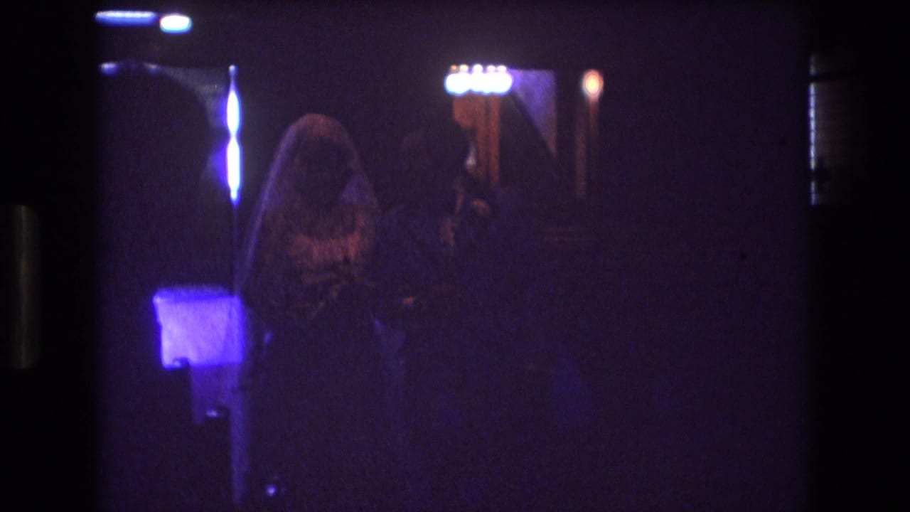 Veiled bride and groom walk through a dim church aisle under purple-blue light.