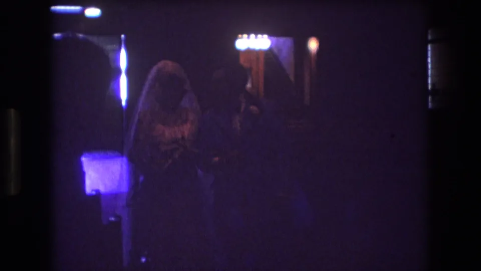In this 1974 Boston 8mm wedding frame, a veiled bride and groom appear in a dark church aisle with stained glass and colored light behind them.