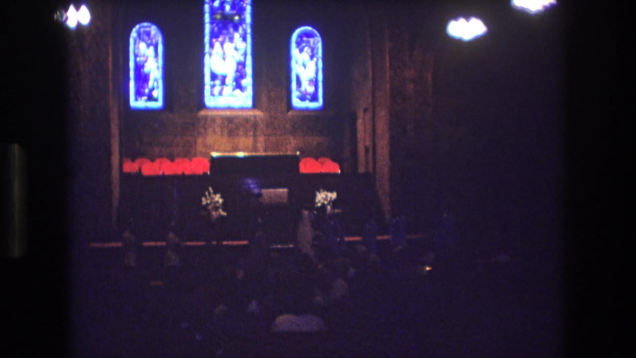 Church altar and stained glass viewed from the aisle in dim light.