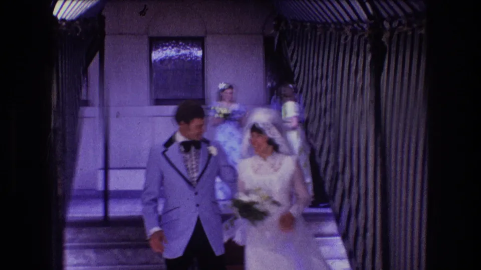 The wedding couple descends exterior steps outside the building, with attendants and striped awning-like edges visible near the entrance.