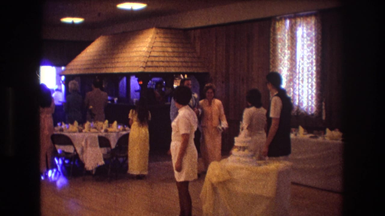 Guests in formal attire move through a banquet room beside a wedding cake table.