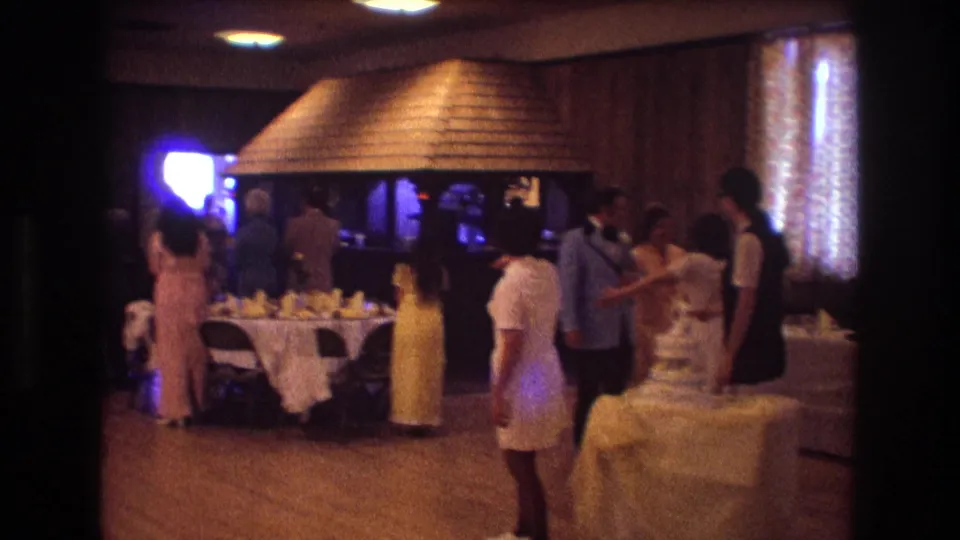 Soft 8mm footage shows 1974 Boston wedding guests mingling in a banquet hall with a cake table and folded napkins visible.