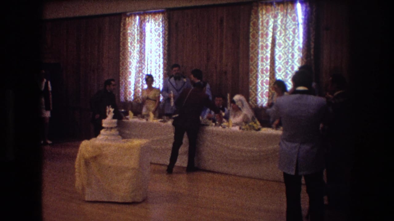 Wedding reception room with the cake table in front and guests gathered around the seated couple.