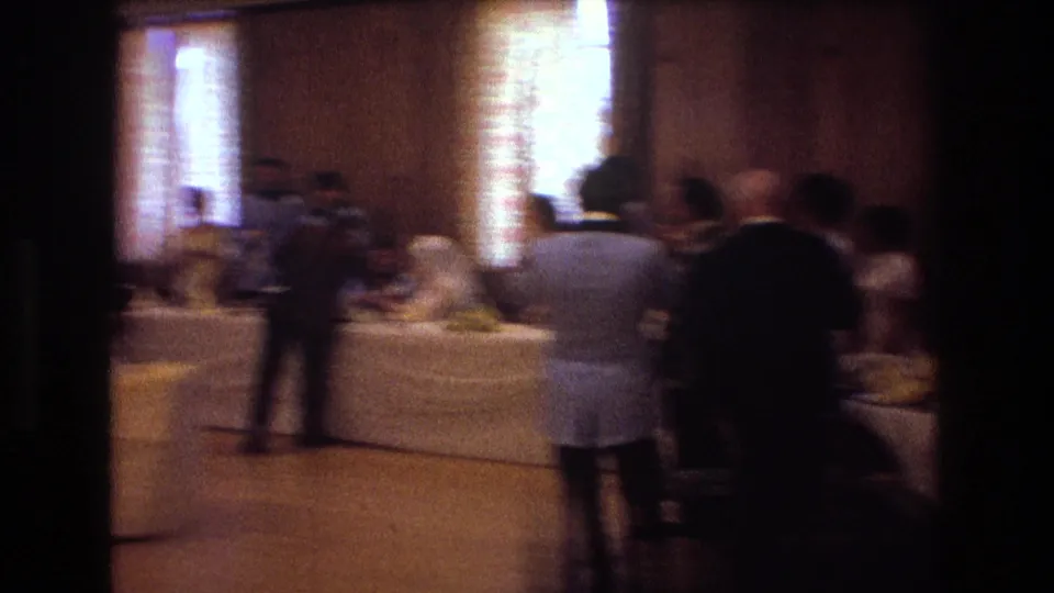 Motion-blurred 8mm frame from the 1974 Boston reception as the camera pans across guests standing near the decorated head table.