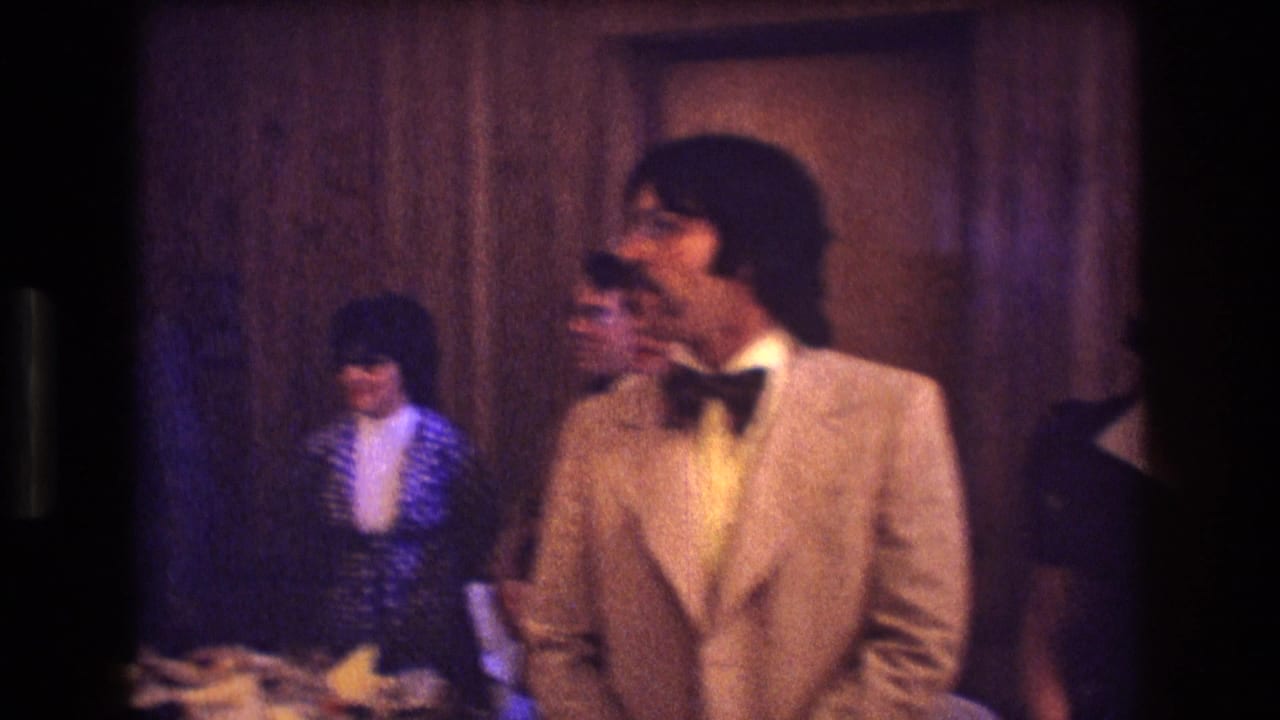 Man in a light suit and bow tie stands among reception guests.
