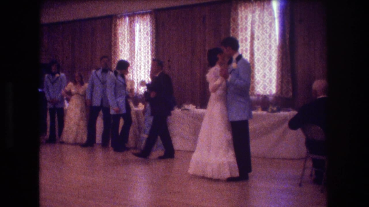 An older man walks near the dancing couple as the wedding party stands by the table.
