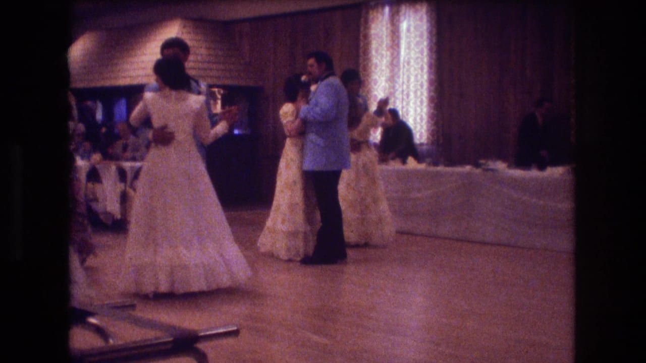A couple waltzes near other wedding guests in a wood-paneled room.