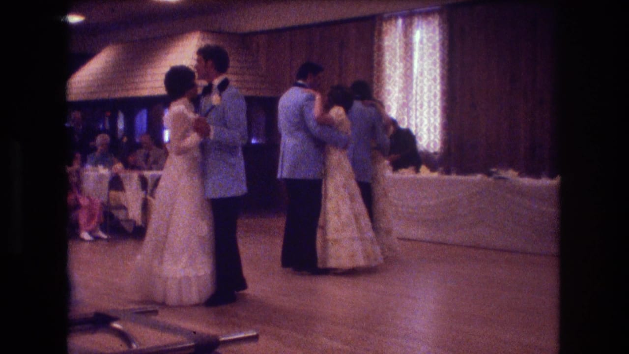Two couples dance near banquet tables and patterned curtains in a reception hall.