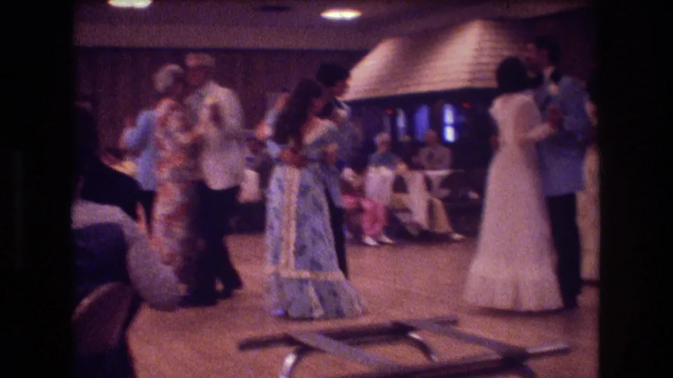 This 1974 Boston home-movie frame captures several reception guests and couples moving across the dance floor, with the bride-like figure at right and seated guests behind.