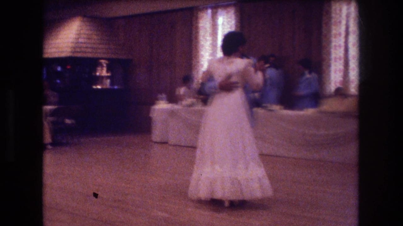 Bride and partner dance in a wood-paneled reception hall while guests sit and stand near banquet tables.