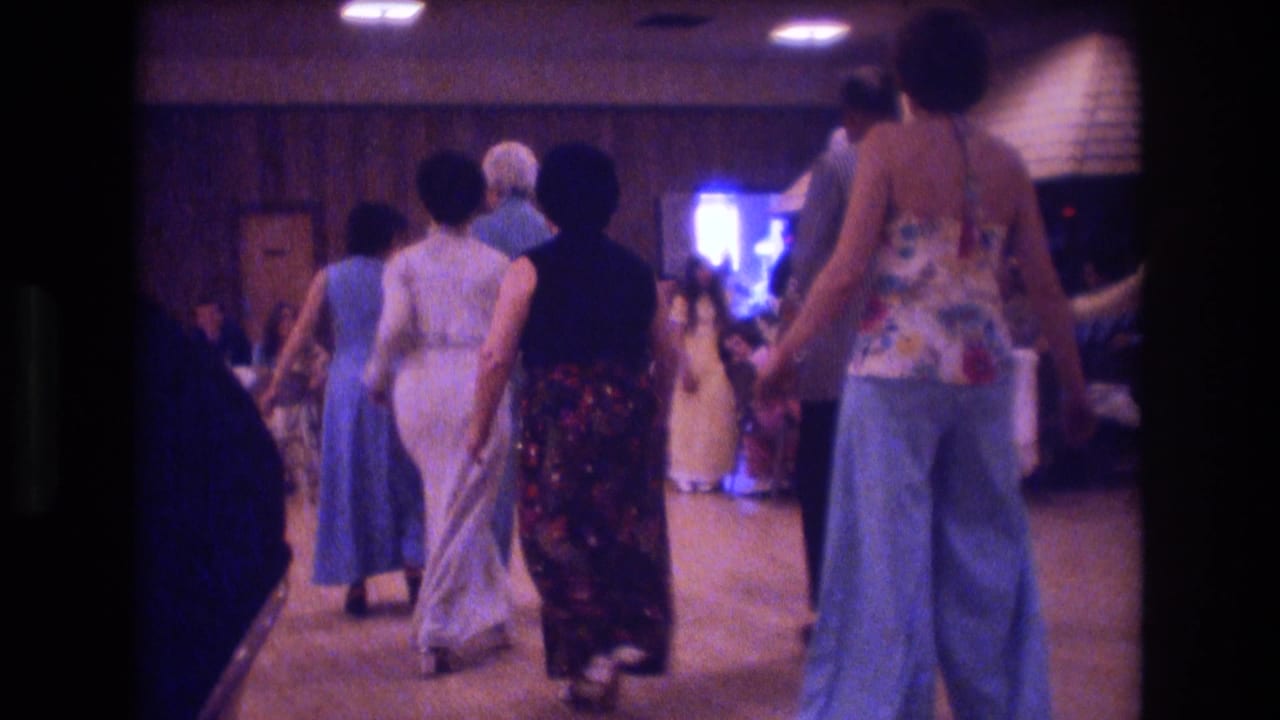 Several women in 1970s-style dresses and wide-leg clothing dance in a dim indoor hall in Boston, according to the clip metadata.