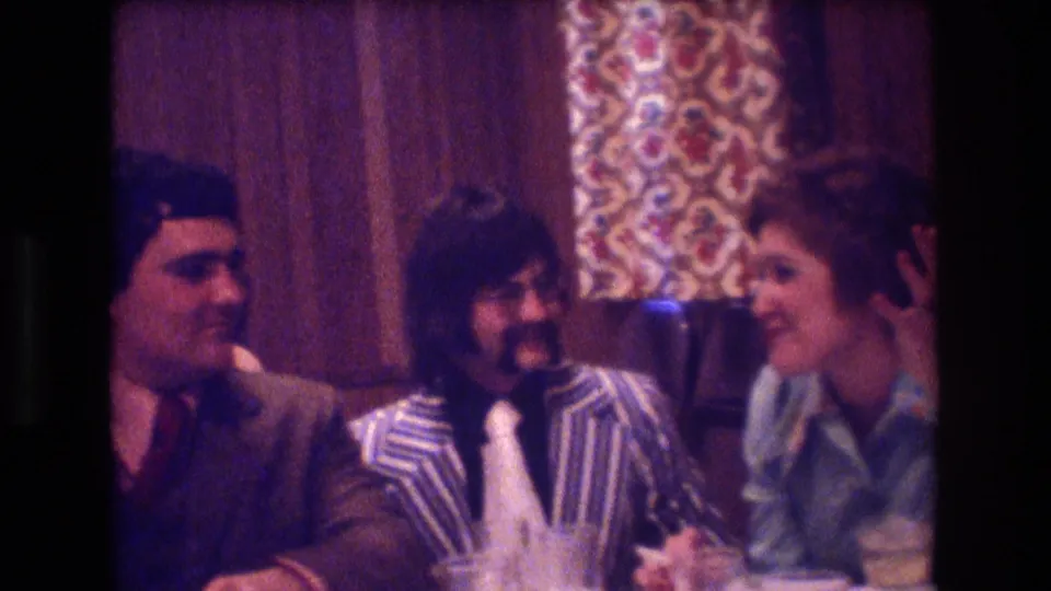 Three adults sit close together at a table in the same wood-paneled interior, smiling and talking during the Boston social gathering indicated by the metadata.