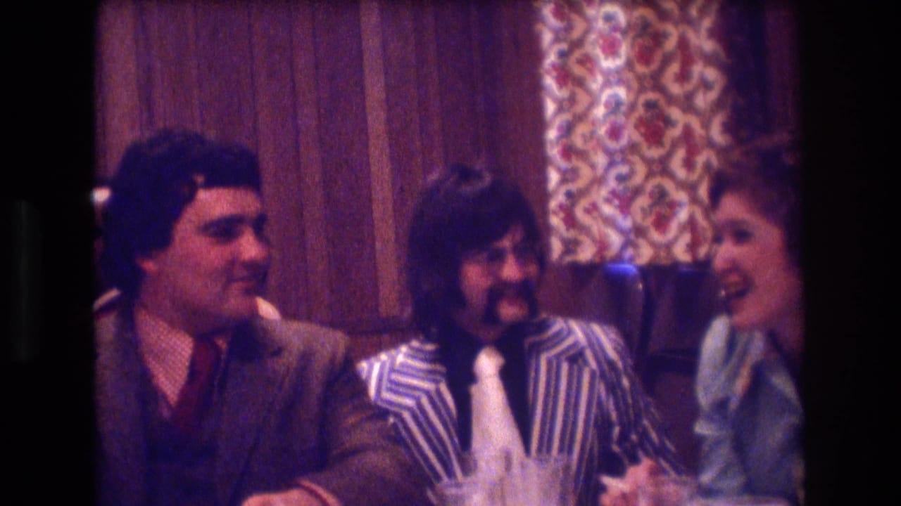 Three adults seated at a restaurant table with wood paneling and patterned curtains behind them.