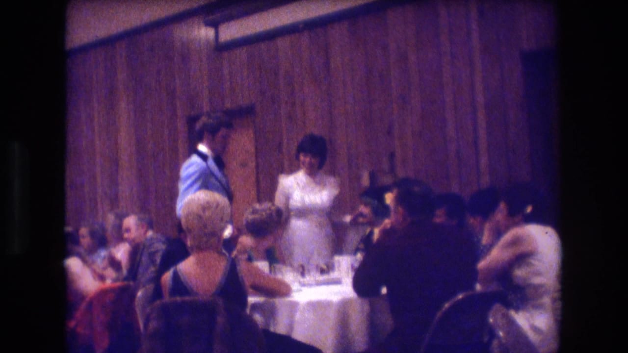 Bride and groom stand near seated guests at a wedding reception table.