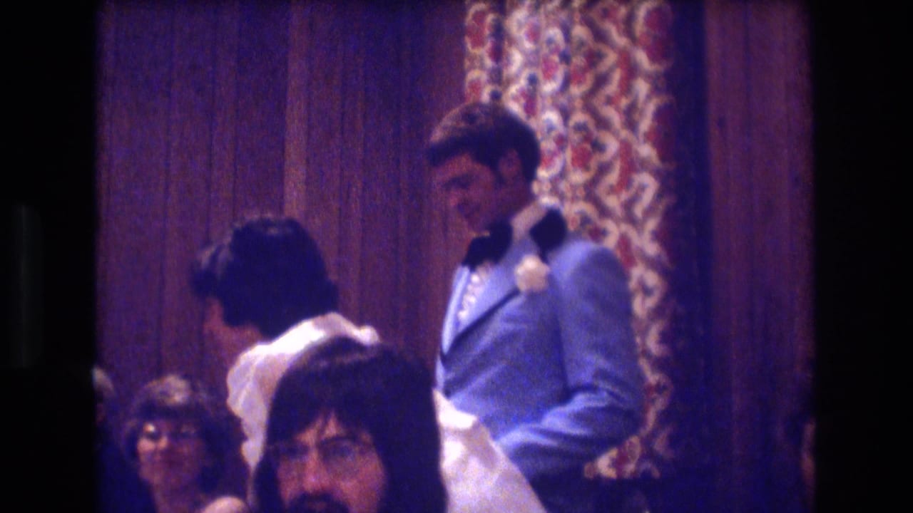 Groom stands beside the bride and seated guests in a banquet room.