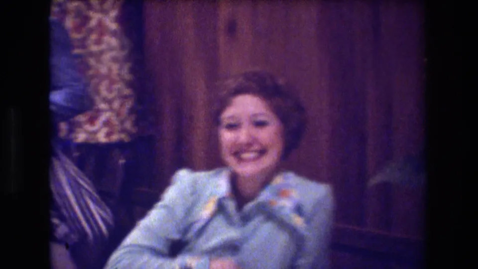 In the final frame, the woman smiles broadly toward the camera in a light blue blouse with a colorful collar, seated against a wood-paneled interior.