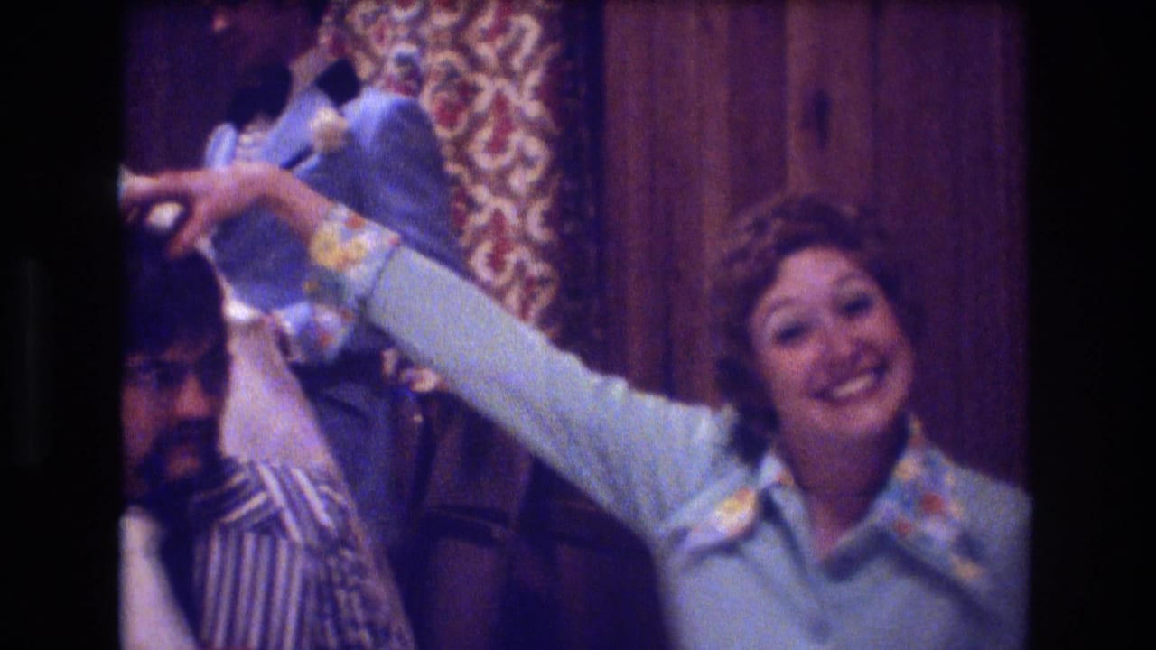 Woman in a light blue dress smiles while reaching toward a seated man during an indoor party.
