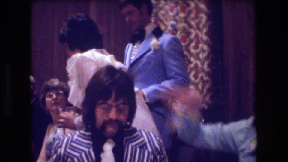 In the indoor Boston party scene, a seated man in a bold striped jacket faces the camera while other adults in formal clothing dance nearby.