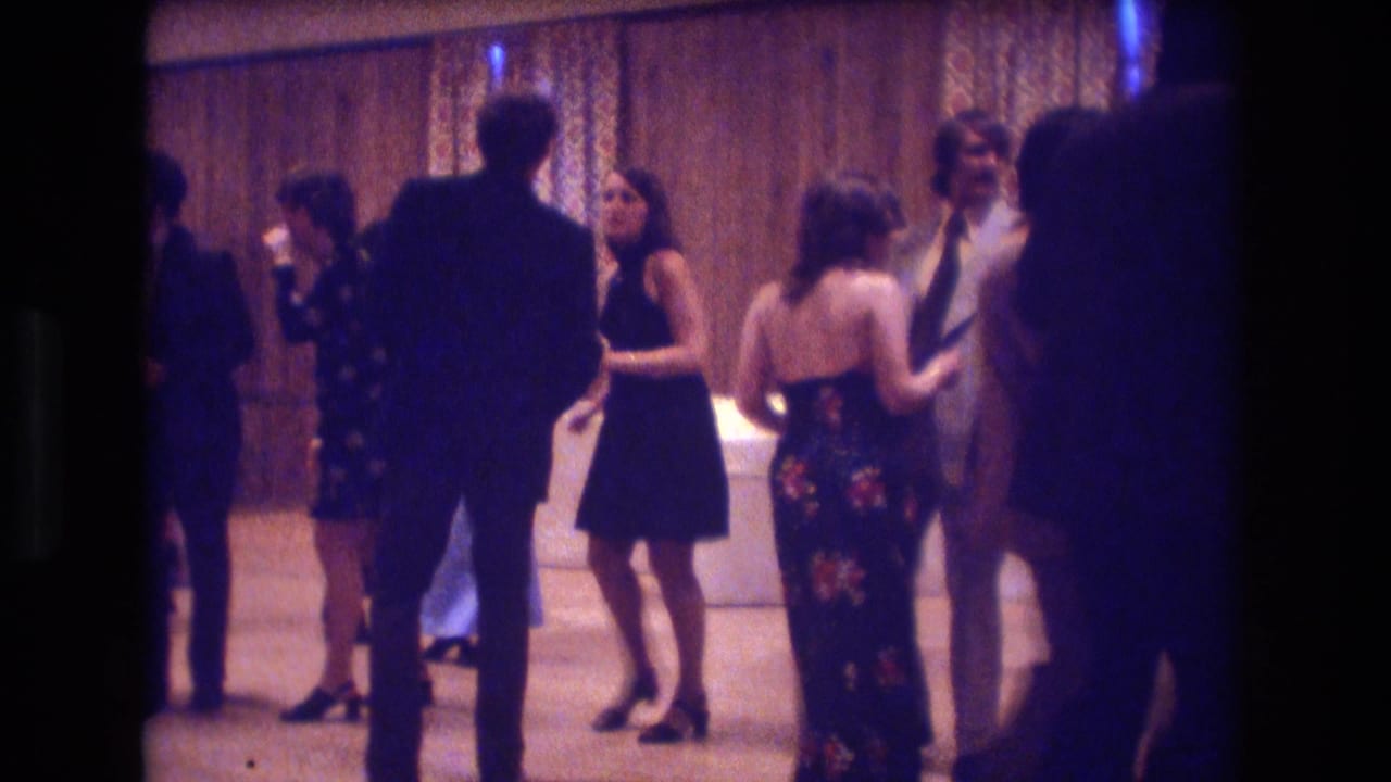 Party guests stand and dance near patterned curtains in a softly lit room.
